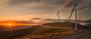 Wind turbines on a hill with the sun setting over the horizon.