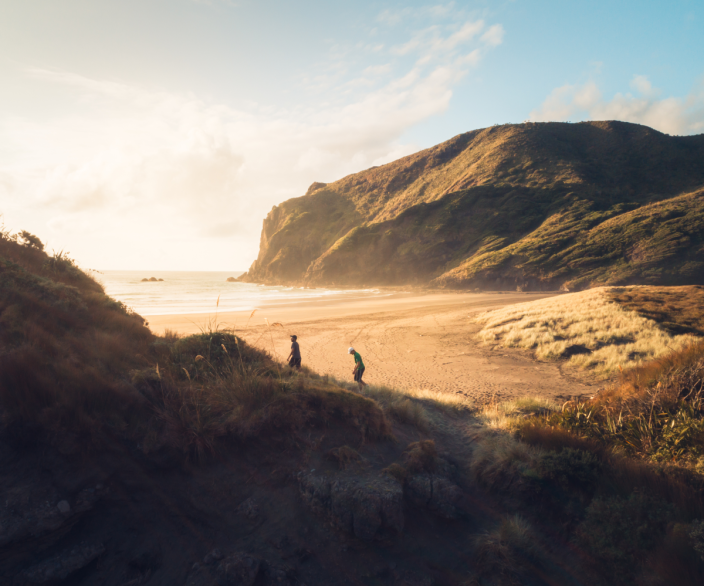 Two people walking on a beach surrounded by mountains.
