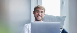 A smiling man using his laptop, relaxed on the couch.