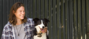 A person laughing while hugging a border collie dog.