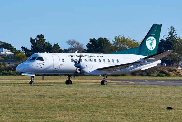 Small regional Air Chathams turboprop airplane on a runway, with trees and buildings in the background.