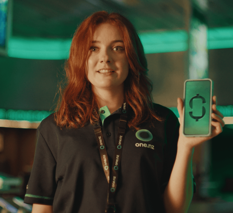 One NZ staff member holds up a smartphone displaying a dollar symbol, representing One Wallet and Phone Dollars.