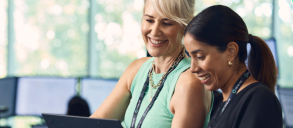 Two women colleagues smiling, looking and pointing at a laptop.