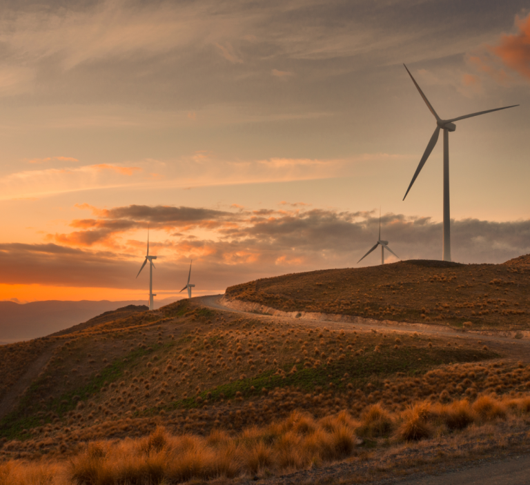 Wind turbines on a hill with the sun setting over the horizon, hinting at the tech involved.